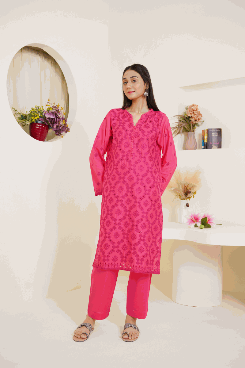 Woman wearing pink lawn embroidered 03-piece suit with matching trousers and dupatta in a room with decorative plants and books